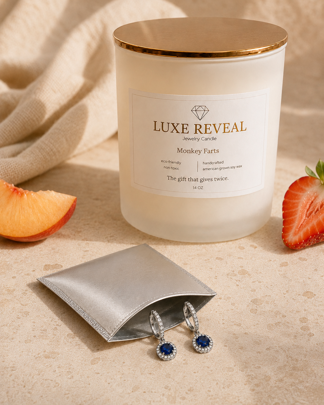 Open silver pouch beside the Monkey Farts Luxe Reveal candle showing the pair of blue sapphire earrings