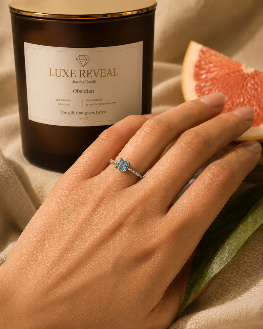 Hand wearing the revealed silver ring with a square aqua gemstone beside the Obsidian Luxe Reveal candle