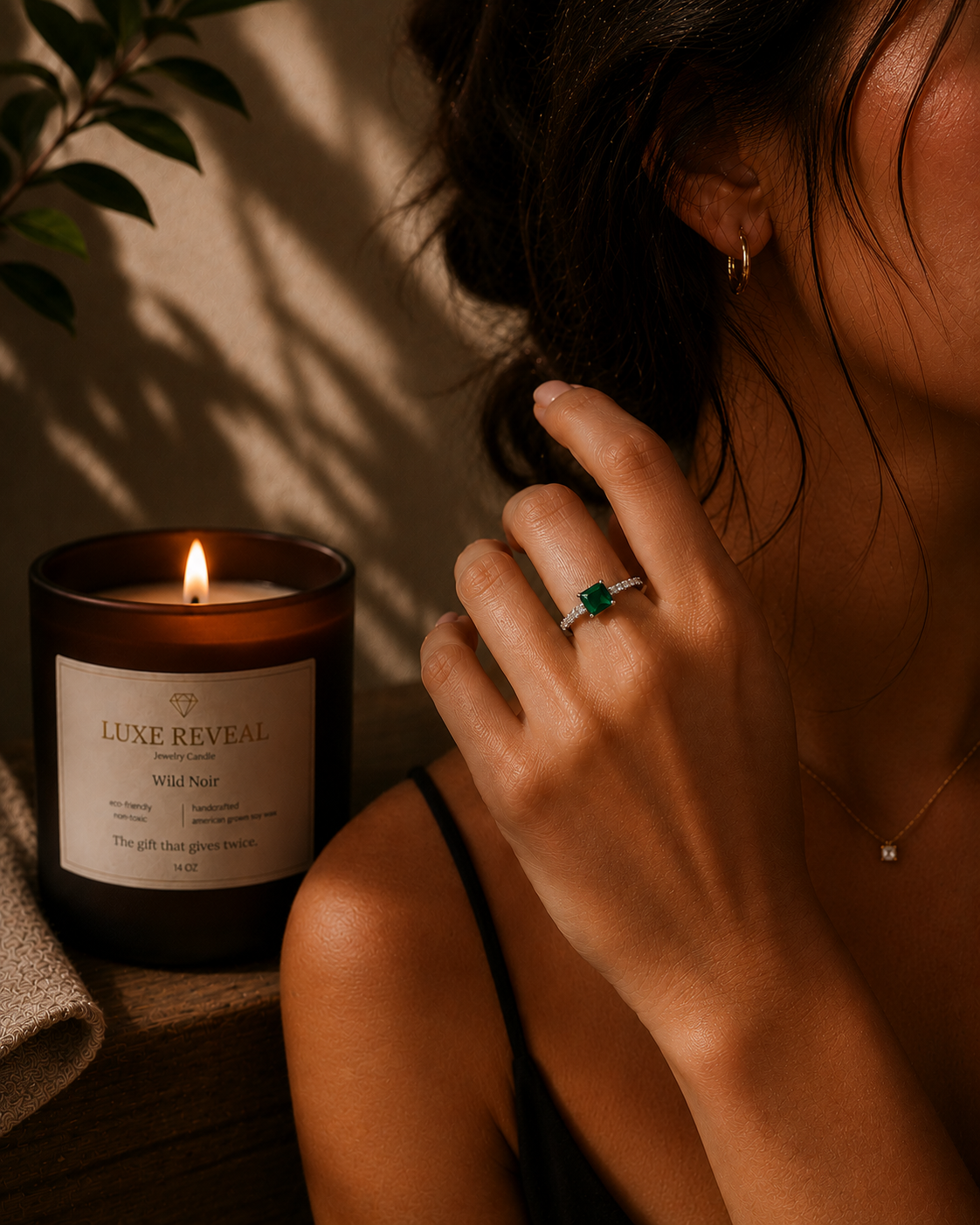 Woman wearing the revealed green gemstone ring with the lit Wild Noir Luxe Reveal candle beside her